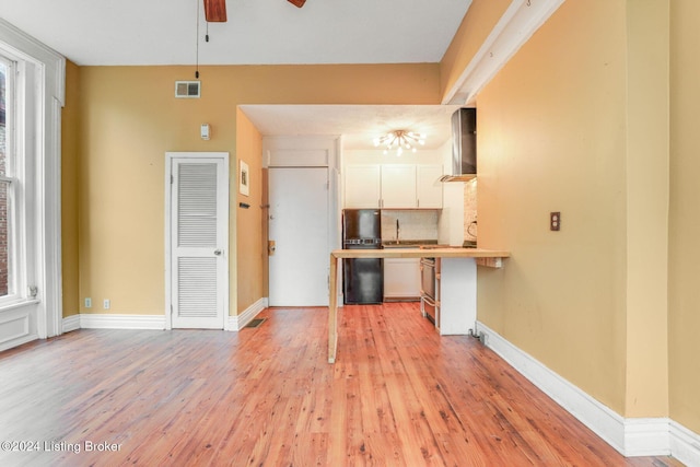 1131 S Brook St Apt 3, Louisville, KY 40203 - kitchen featuring wall chimney exhaust hood, a ceiling fan, freestanding refrigerator, white cabinets, and light wood-style flooring