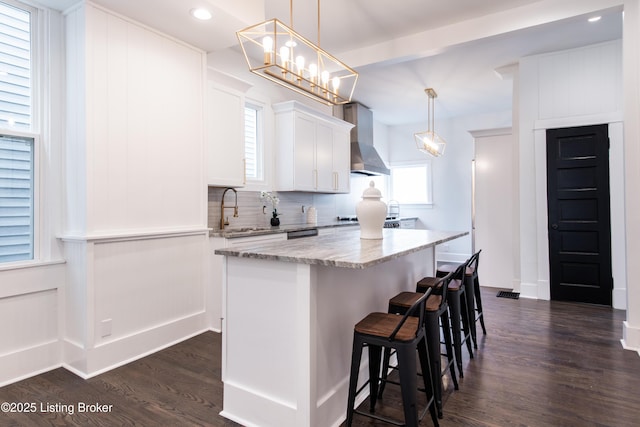 1293 Everett Ave, Louisville, KY 40204 - kitchen featuring wall chimney exhaust hood, backsplash, light stone countertops, a kitchen island, and dark wood finished floors