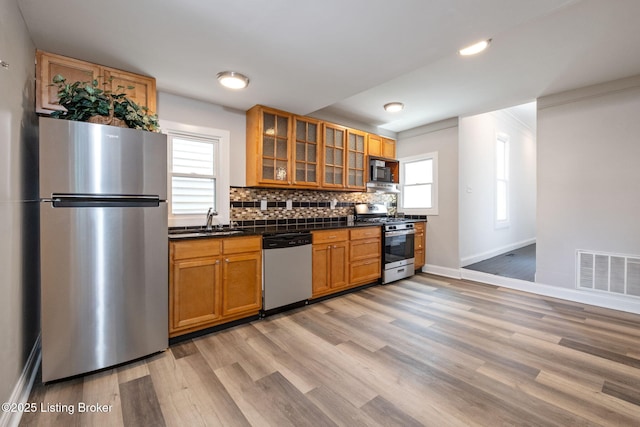 631 Lynn St, Louisville, KY 40217 - kitchen featuring appliances with stainless steel finishes, dark countertops, light wood-style flooring, brown cabinets, and plenty of natural light