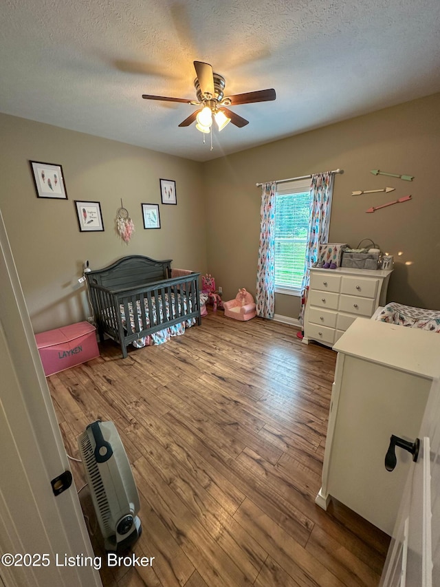 68 Lonnie Lawson Ct, Brandenburg, KY 40108 - bedroom featuring a nursery area, wood finished floors, a textured ceiling, and a ceiling fan