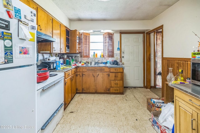 911 N Main St, Barbourville, KY 40906 - kitchen featuring white appliances, under cabinet range hood, a wainscoted wall, a textured ceiling, and brown cabinetry