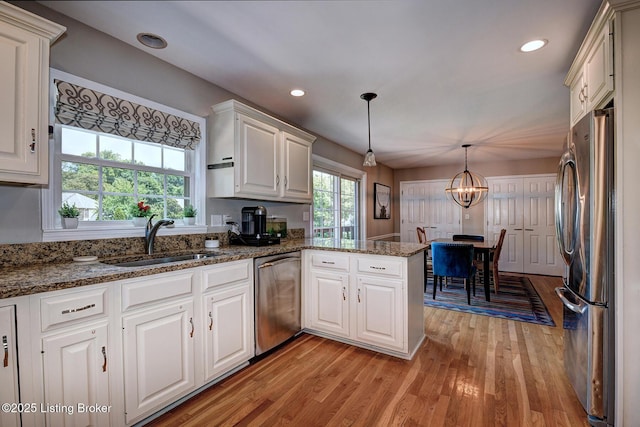 6011 Windsong Ct, Louisville, KY 40207 - kitchen featuring appliances with stainless steel finishes, a peninsula, light wood-style flooring, white cabinetry, and decorative light fixtures