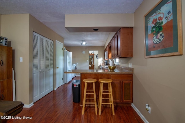 933 Lakeshore Pkwy, Brandenburg, KY 40108 - kitchen with dark wood-style floors, brown cabinetry, a peninsula, white fridge with ice dispenser, and a breakfast bar area