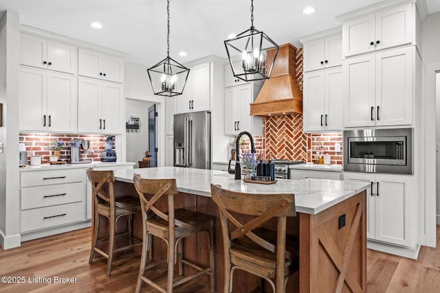 2070 Tonieville Rd, Hodgenville, KY 42748 - kitchen featuring appliances with stainless steel finishes, custom exhaust hood, tasteful backsplash, a chandelier, and a kitchen island with sink