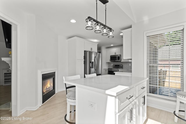 5613 Grandel Blvd, Louisville, KY 40258 - kitchen featuring stainless steel appliances, a glass covered fireplace, light wood-style flooring, white cabinets, and healthy amount of natural light