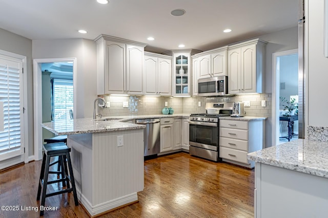 17503 Polo Run Ln, Louisville, KY 40245 - kitchen featuring stainless steel appliances, a peninsula, glass insert cabinets, light stone counters, and a kitchen bar