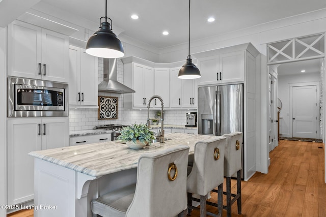 6331 Mistflower Cir, Prospect, KY 40059 - kitchen featuring appliances with stainless steel finishes, wall chimney range hood, tasteful backsplash, a kitchen island with sink, and light wood-type flooring