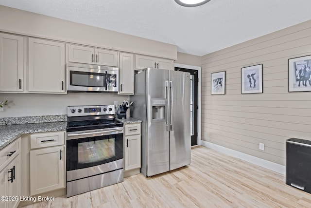 508 Auburn Oaks Dr, Louisville, KY 40214 - kitchen with appliances with stainless steel finishes, wood walls, light wood-style flooring, light stone counters, and a textured ceiling