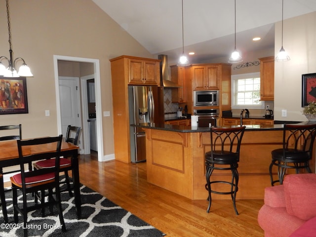 193 Pare Ct, Shepherdsville, KY 40165 - kitchen featuring appliances with stainless steel finishes, wall chimney range hood, wood finished floors, dark countertops, and a kitchen bar