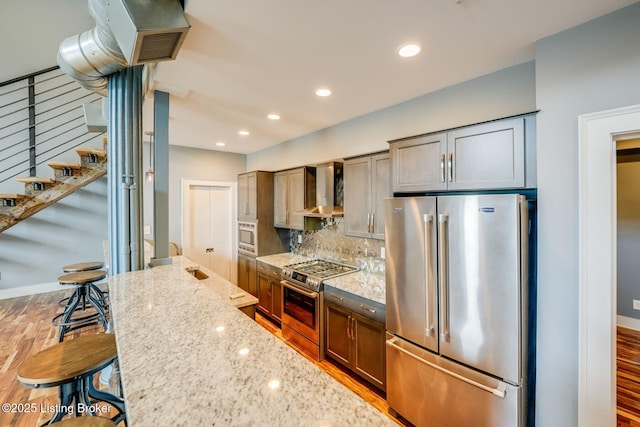 415 E Market St Unit 104, Louisville, KY 40202 - kitchen with stainless steel appliances, wall chimney exhaust hood, a kitchen breakfast bar, light stone countertops, and tasteful backsplash