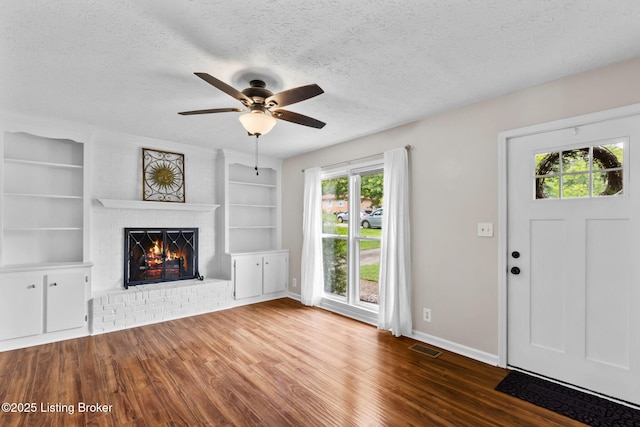 6818 Village Green Blvd, Pewee Valley, KY 40056 - unfurnished living room featuring a textured ceiling, a brick fireplace, wood finished floors, built in shelves, and a ceiling fan