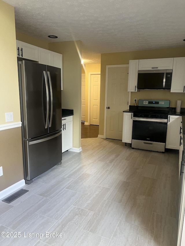 9403 Alex Ct, Louisville, KY 40299 - kitchen featuring appliances with stainless steel finishes, white cabinetry, dark countertops, a textured ceiling, and light wood-style flooring