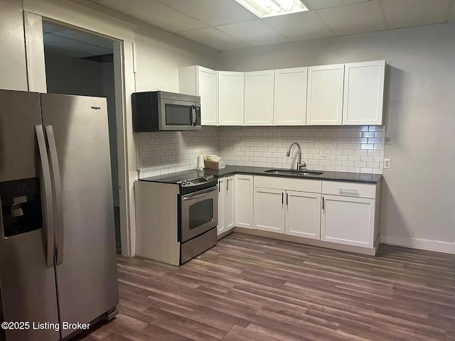 1214 Logan St, Louisville, KY 40204 - kitchen with appliances with stainless steel finishes, dark countertops, dark wood-type flooring, white cabinets, and backsplash