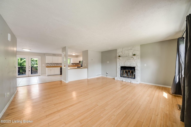 2700 Pioneer Ct, Radcliff, KY 40160 - unfurnished living room with a textured ceiling, light wood-style floors, a stone fireplace, and french doors