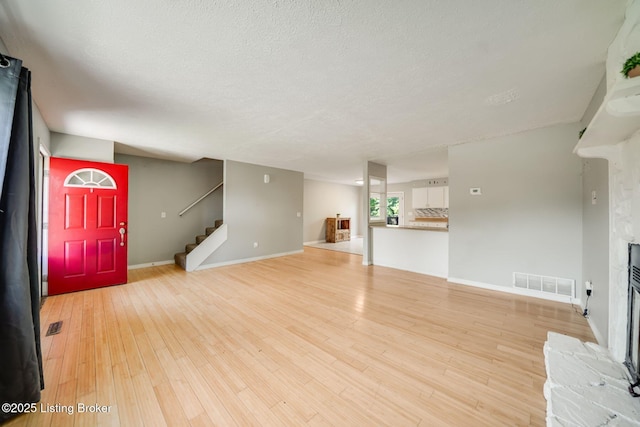 2700 Pioneer Ct, Radcliff, KY 40160 - unfurnished living room featuring light wood finished floors, a fireplace, stairway, and a textured ceiling