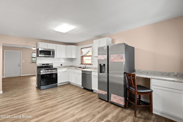 3322 Virginia Ave, Louisville, KY 40211 - kitchen with appliances with stainless steel finishes, light wood-style floors, decorative backsplash, white cabinets, and light countertops