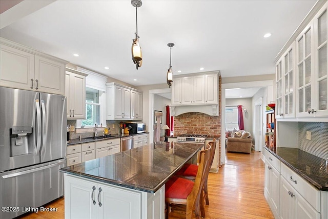 2449 Ransdell Ave, Louisville, KY 40204 - kitchen featuring appliances with stainless steel finishes, decorative backsplash, light wood-type flooring, a center island, and glass insert cabinets