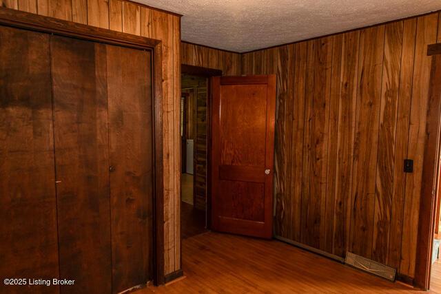 4883 S Reeves Rd, Scottsburg, IN 47170 - unfurnished bedroom featuring a textured ceiling, wooden walls, a closet, and wood finished floors