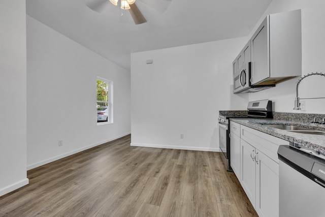 kitchen with light wood finished floors, appliances with stainless steel finishes, a sink, and baseboards