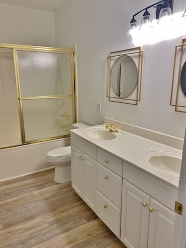 full bathroom with shower / bath combination with glass door, hardwood / wood-style floors, vanity, and toilet