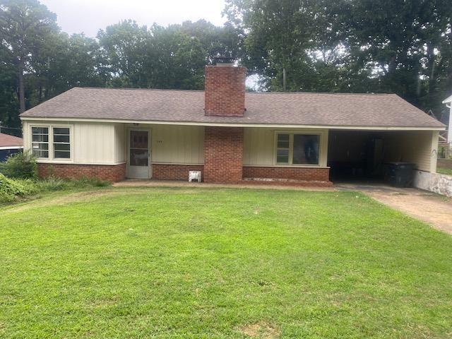  - ranch-style house featuring a chimney, brick siding, a front yard, and concrete driveway