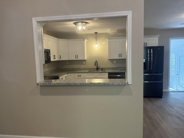 kitchen with sink, light stone counters, pendant lighting, white cabinets, and black appliances