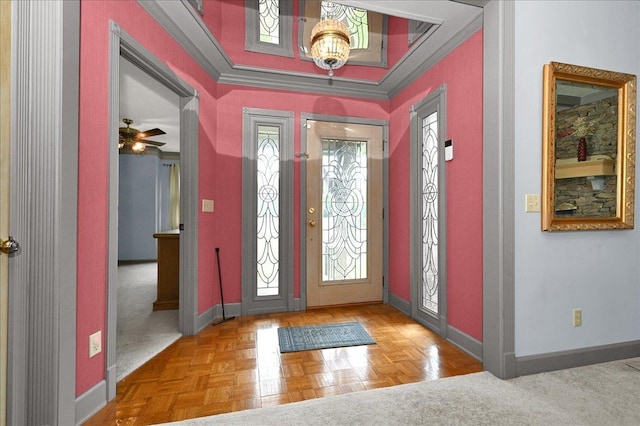 foyer with ornamental molding, ceiling fan with notable chandelier, and parquet flooring