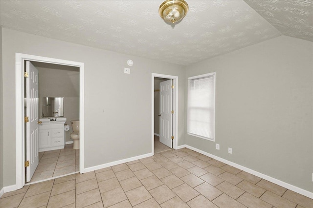 unfurnished bedroom featuring connected bathroom, lofted ceiling, light tile patterned floors, and a textured ceiling