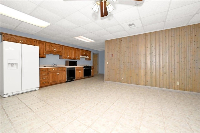 kitchen with a paneled ceiling, ceiling fan, sink, black appliances, and wood walls