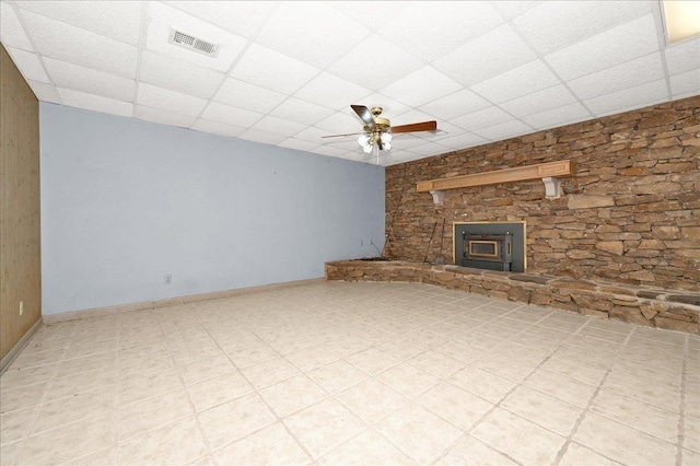 unfurnished living room featuring a paneled ceiling, ceiling fan, and a wood stove