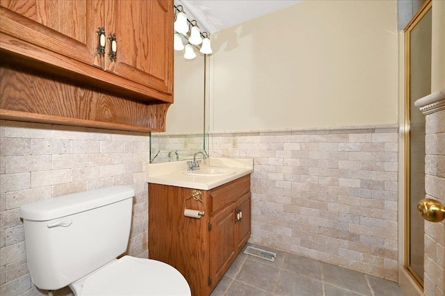 bathroom featuring vanity, toilet, walk in shower, and tile walls