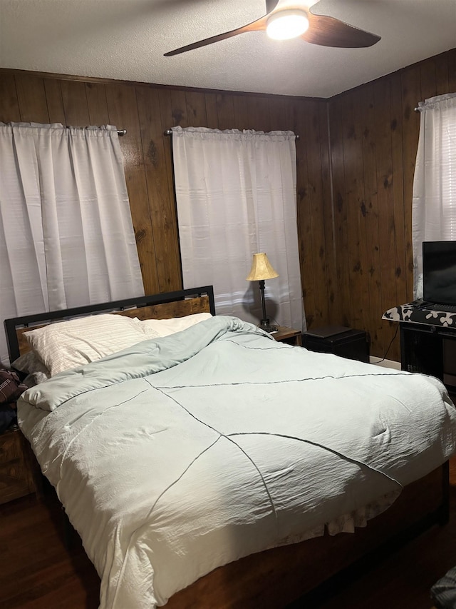 bedroom with a textured ceiling, ceiling fan, and wooden walls