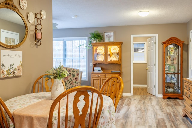 dining room featuring baseboards, a textured ceiling, and light wood finished floors