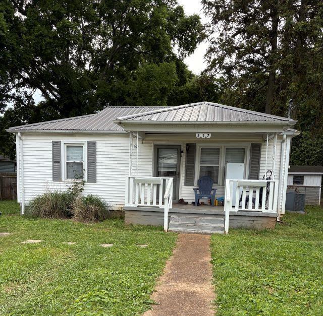 - view of front facade featuring a front yard, a porch, and metal roof