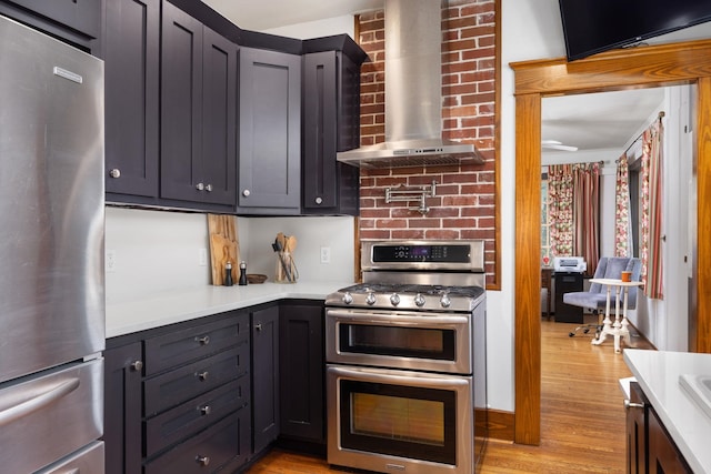 kitchen featuring stainless steel appliances, wall chimney range hood, light countertops, and light wood-style flooring