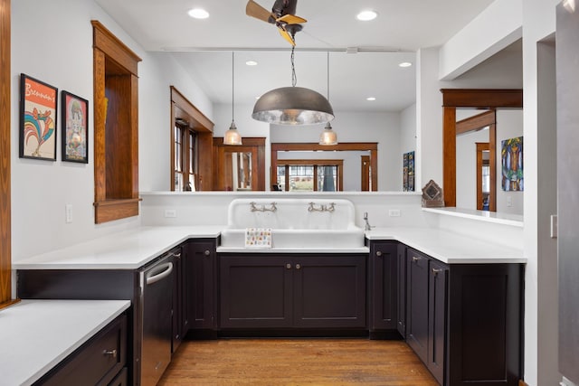 kitchen with light countertops, hanging light fixtures, light wood-style flooring, a sink, and a peninsula