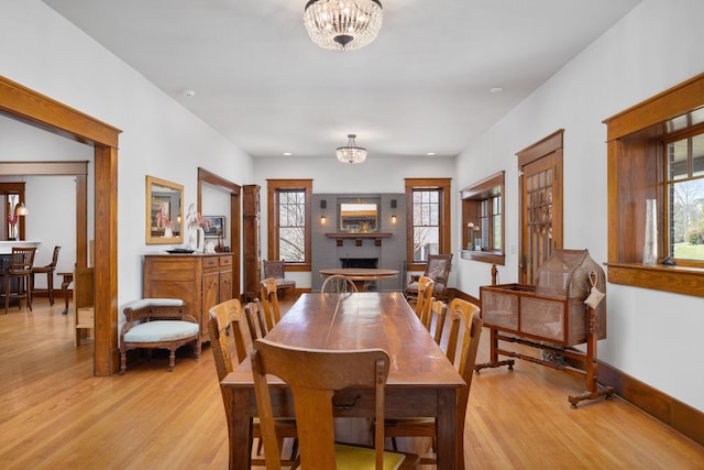 dining space featuring a healthy amount of sunlight, light wood-style flooring, a fireplace, and a chandelier