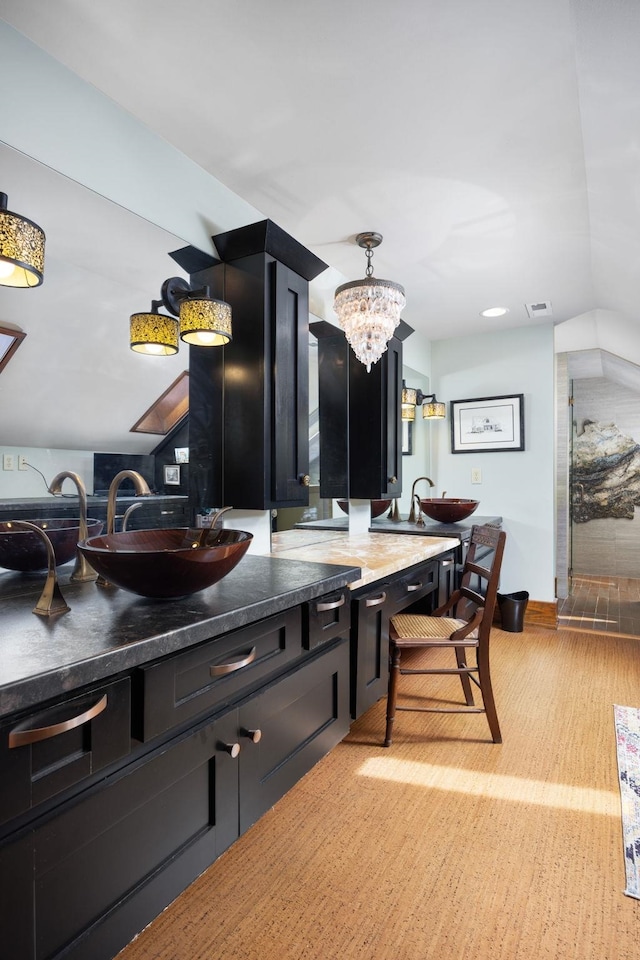 kitchen with decorative light fixtures, light wood finished floors, dark countertops, a sink, and dark cabinetry