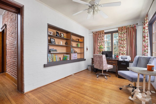 office area featuring built in shelves, crown molding, a ceiling fan, brick wall, and light wood-type flooring