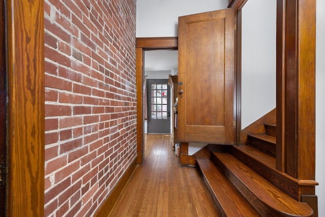 hall featuring brick wall, stairs, and wood finished floors