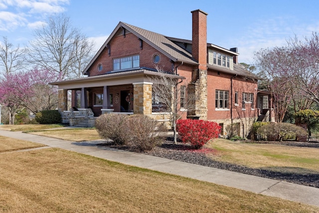 view of front of home featuring brick siding, a chimney, covered porch, stone siding, and a front lawn