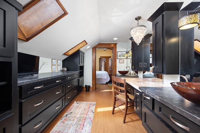 kitchen featuring dark cabinets, dark countertops, pendant lighting, and vaulted ceiling with skylight