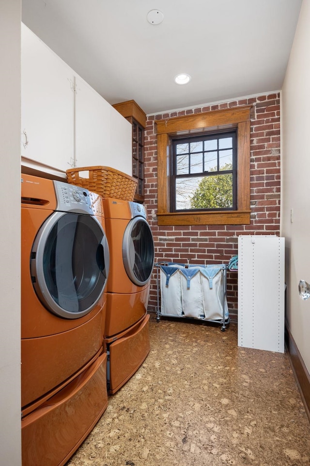 washroom with cabinet space, baseboards, brick wall, washing machine and dryer, and recessed lighting