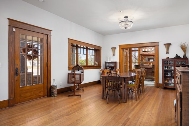 dining space featuring light wood-style floors, a fireplace, a notable chandelier, and baseboards