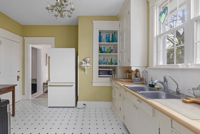  - kitchen with freestanding refrigerator, a sink, light countertops, stainless steel microwave, and baseboards