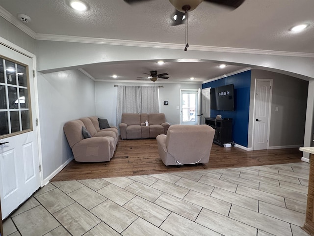 living room featuring ornamental molding, light wood-type flooring, a textured ceiling, and ceiling fan