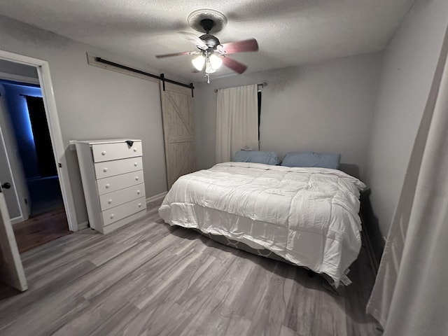 bedroom with ceiling fan, a barn door, light hardwood / wood-style flooring, and a textured ceiling