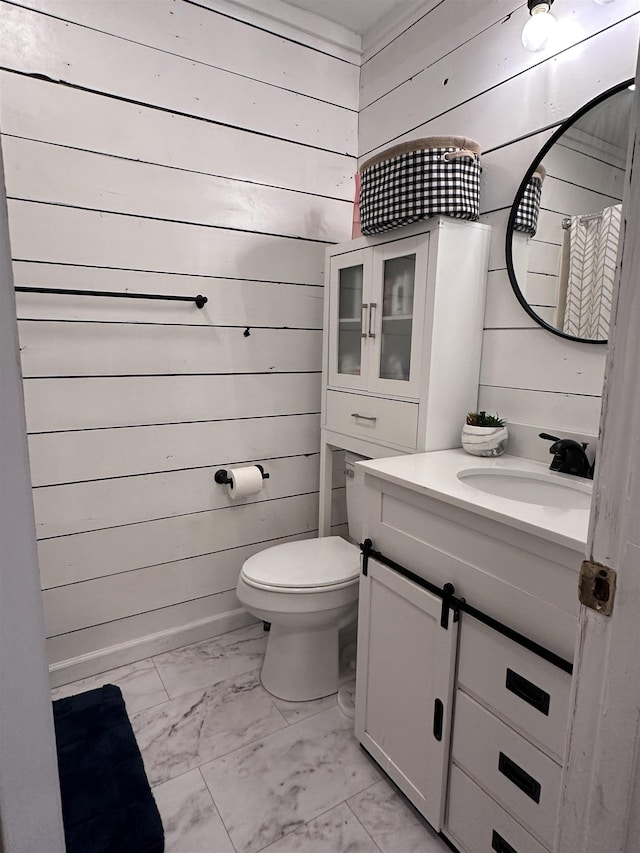 bathroom featuring toilet, vanity, and wooden walls