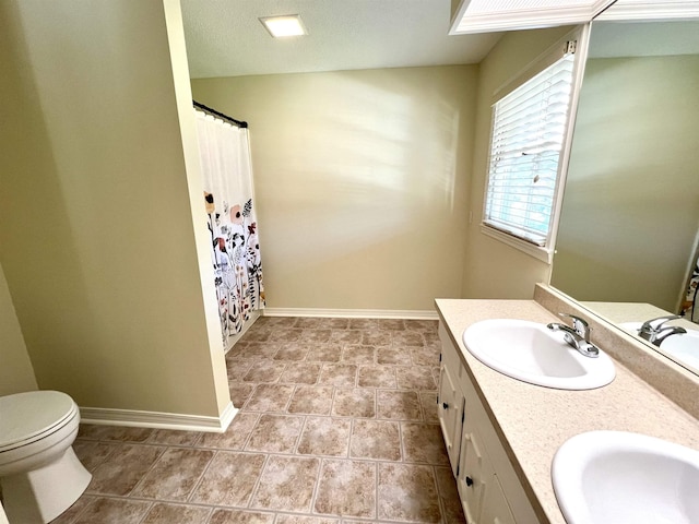 full bathroom with double vanity, baseboards, toilet, and a sink