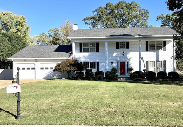 greek revival inspired property featuring a front yard, a chimney, and an attached garage